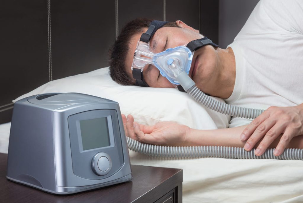 Man sleeping on bed while hooked up to a CPAP machine.