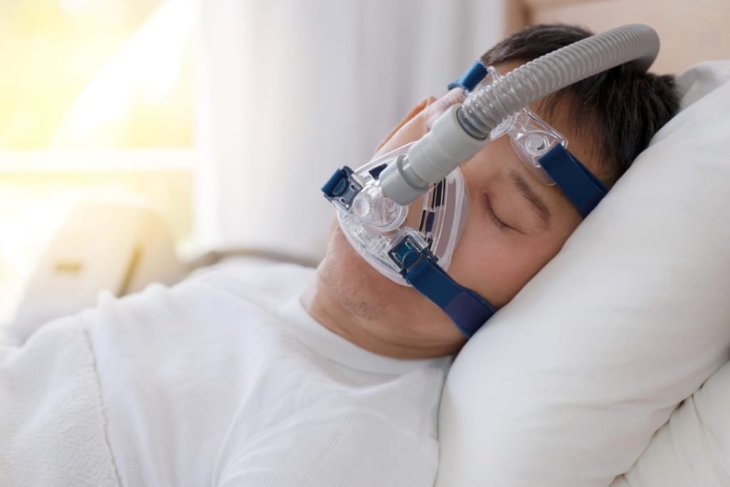 Man in bed wearing a CPAP machine.